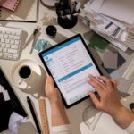 Przedsiębiorca potwierdzający wysyłkę faktury na tablecie obok laptopa