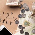 Widok z góry na biurko z pieniędzmi w róznych walutach, dokumentami i kalkulatorem używanymi do przeliczania kursów walut