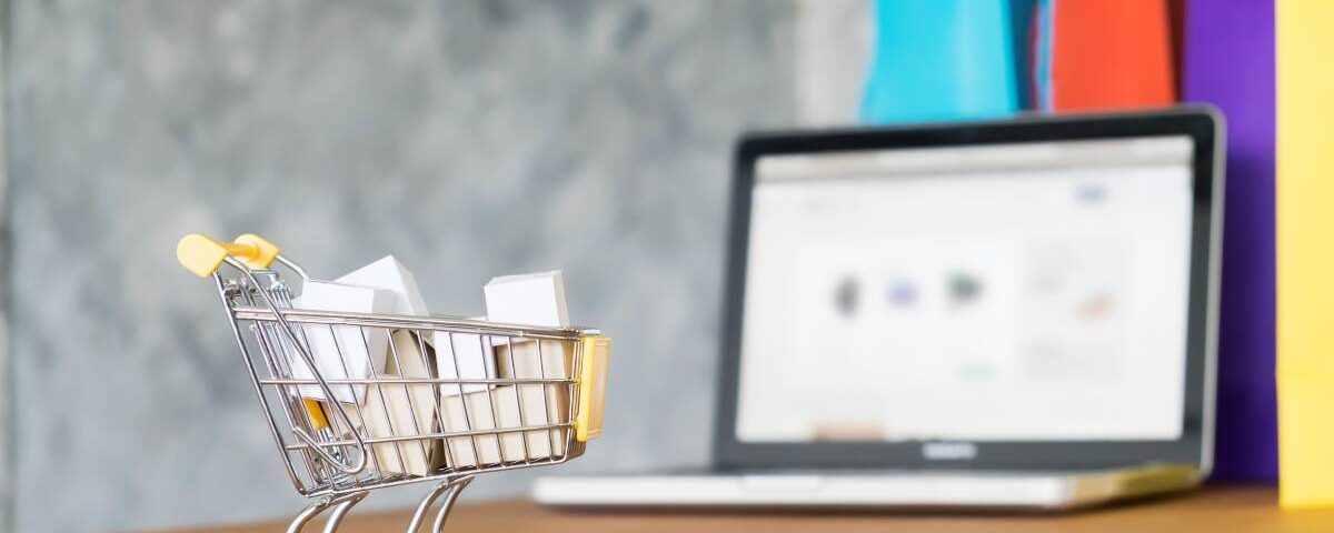 Wózek zakupowy z paczkami ustawiony przed laptopem jako metafora sprzedaży na platformach typu marketplace