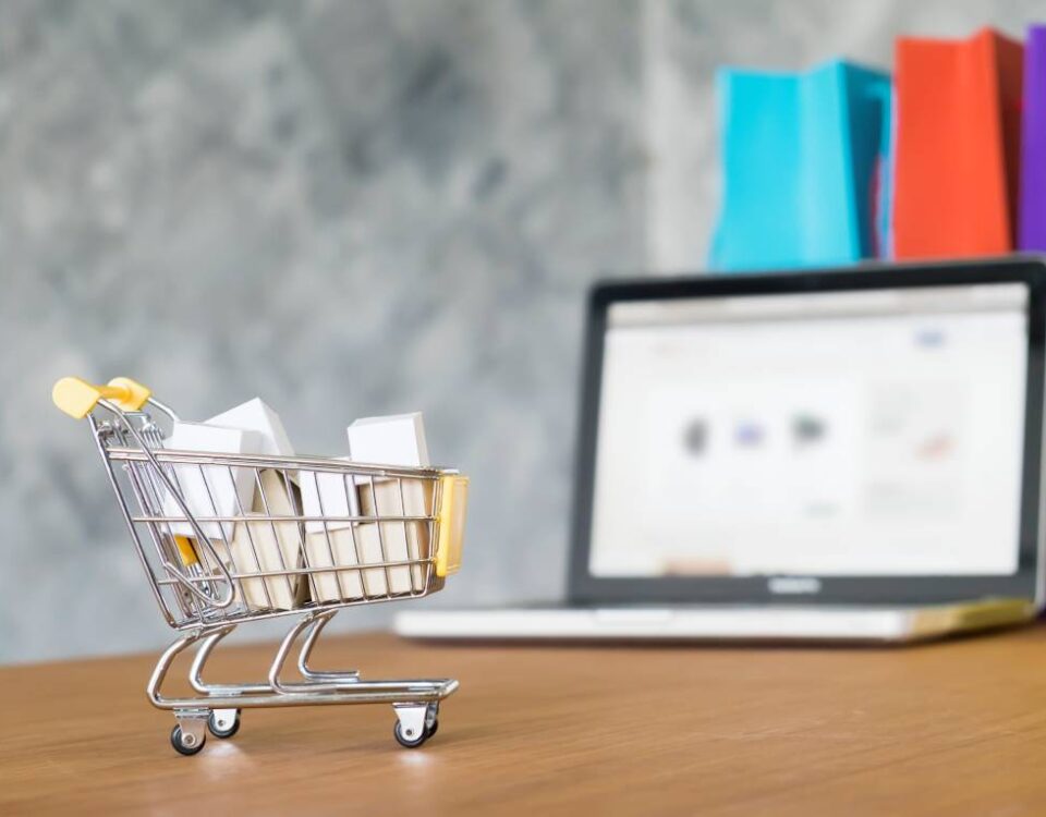 Wózek zakupowy z paczkami ustawiony przed laptopem jako metafora sprzedaży na platformach typu marketplace