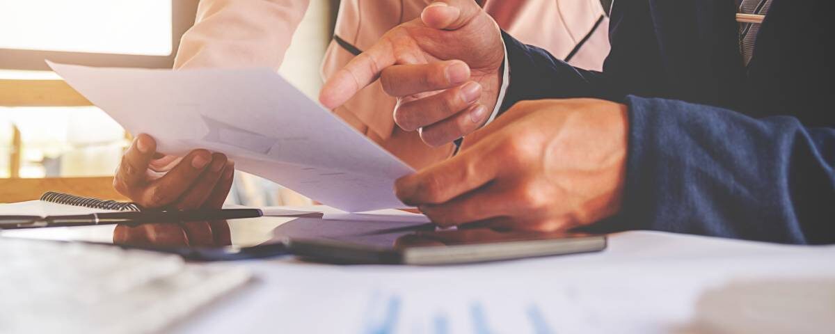 Zbliżenie na ręce dwóch osób omawiających dokumenty finansowe, symbolizujące analizę długoterminowych skutków estońskiego CIT