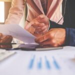 Zbliżenie na ręce dwóch osób omawiających dokumenty finansowe, symbolizujące analizę długoterminowych skutków estońskiego CIT