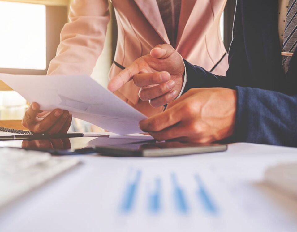 Zbliżenie na ręce dwóch osób omawiających dokumenty finansowe, symbolizujące analizę długoterminowych skutków estońskiego CIT