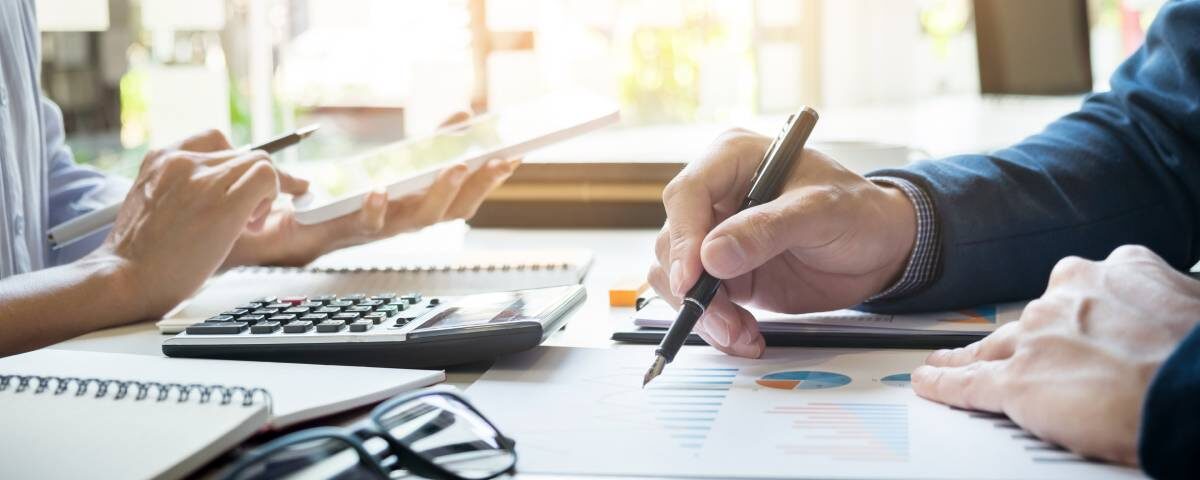 Zbliżenie na biurko księgowe, ręka księgowego zaznaczająca dane na dokumentach, komputer i akcesoria używane przy rozliczeniach estońskiego CIT