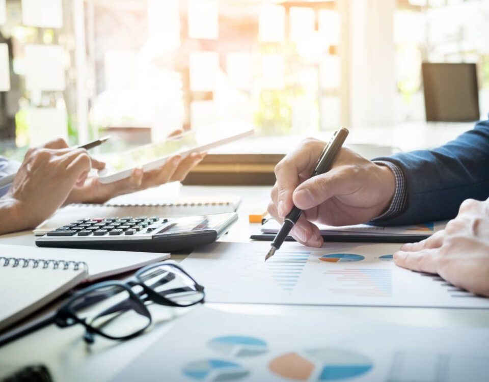 Zbliżenie na biurko księgowe, ręka księgowego zaznaczająca dane na dokumentach, komputer i akcesoria używane przy rozliczeniach estońskiego CIT